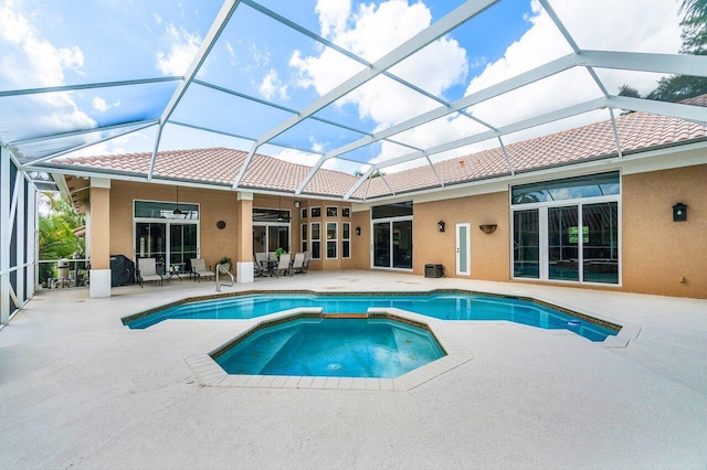 view of swimming pool with glass enclosure, ceiling fan, a patio, and an in ground hot tub