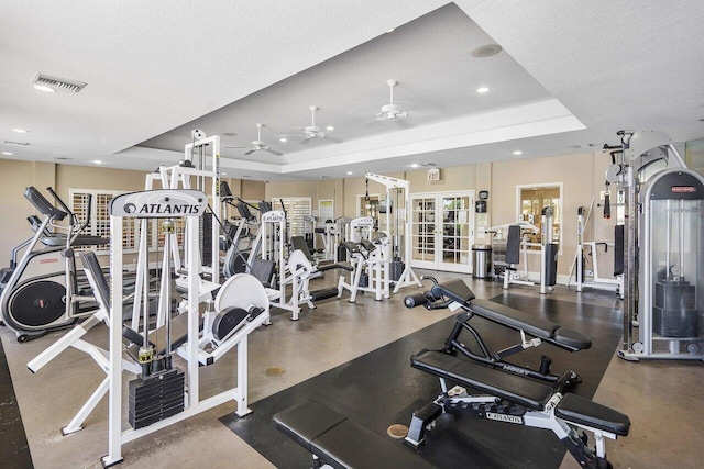 workout area with a textured ceiling, ceiling fan, and a raised ceiling