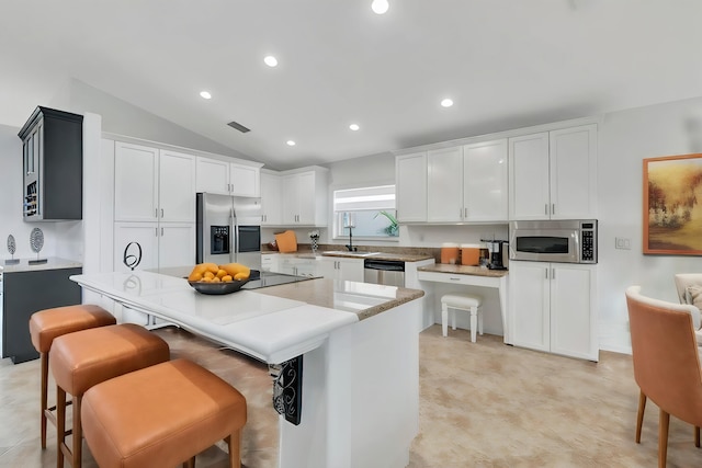 kitchen featuring a kitchen breakfast bar, a center island, stainless steel appliances, and vaulted ceiling