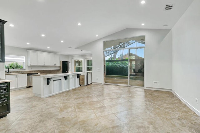 kitchen featuring lofted ceiling, a kitchen breakfast bar, white cabinetry, dishwasher, and a center island