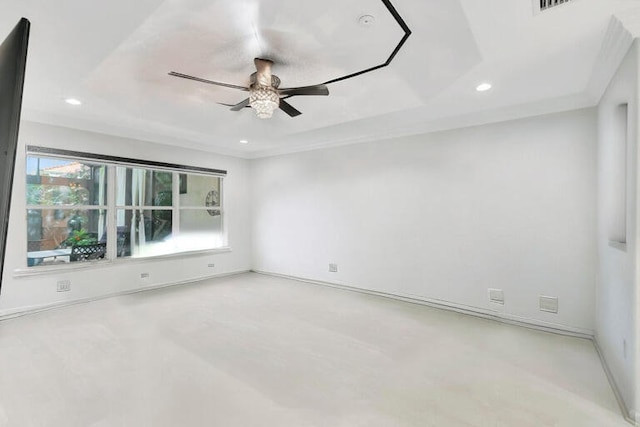 spare room featuring light carpet, a tray ceiling, and ceiling fan