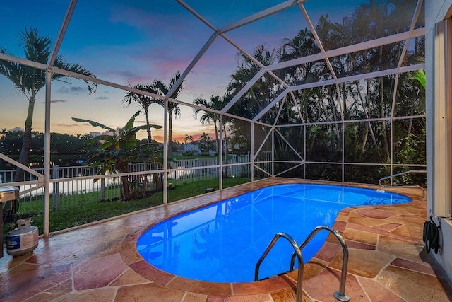 pool at dusk featuring glass enclosure and a patio area