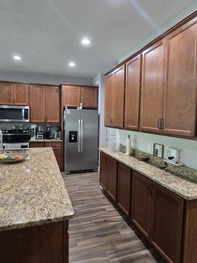 kitchen with light stone counters, a textured ceiling, appliances with stainless steel finishes, and dark wood-type flooring