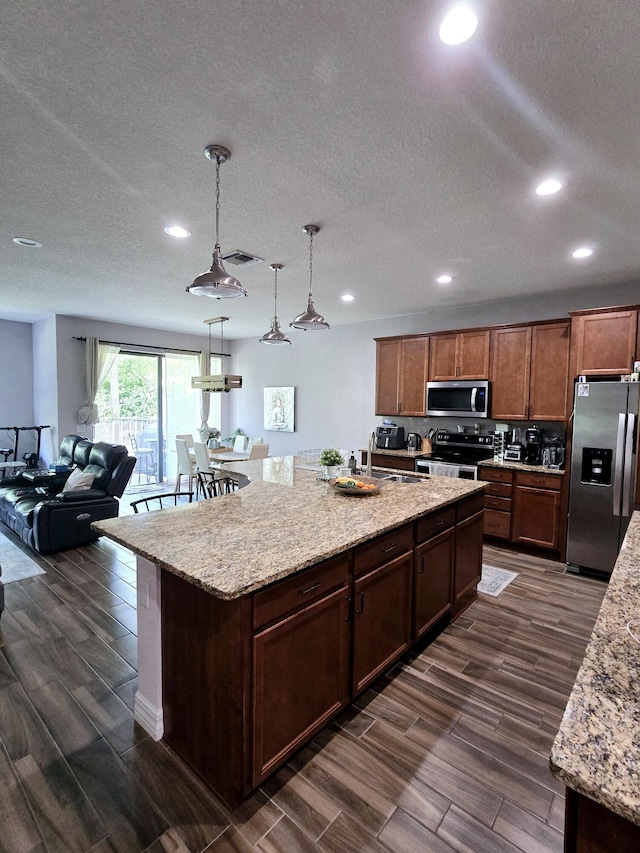 kitchen featuring an island with sink, dark hardwood / wood-style floors, pendant lighting, and stainless steel appliances