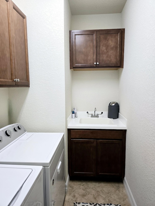 clothes washing area with light tile patterned floors, sink, washing machine and clothes dryer, and cabinets