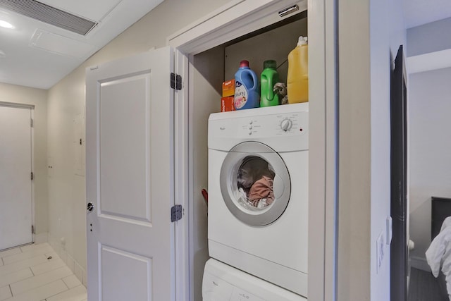 laundry area with light tile patterned flooring and stacked washing maching and dryer