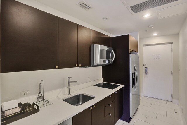 kitchen with appliances with stainless steel finishes, dark brown cabinetry, light tile patterned flooring, and sink