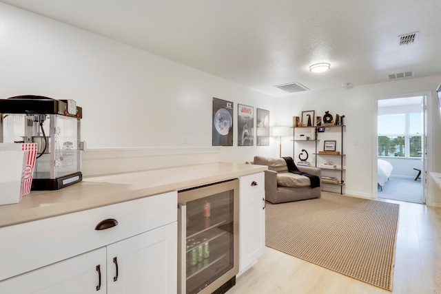 bar with white cabinets, light wood-type flooring, and beverage cooler