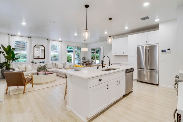 kitchen with a kitchen island with sink, stainless steel appliances, sink, decorative light fixtures, and white cabinetry