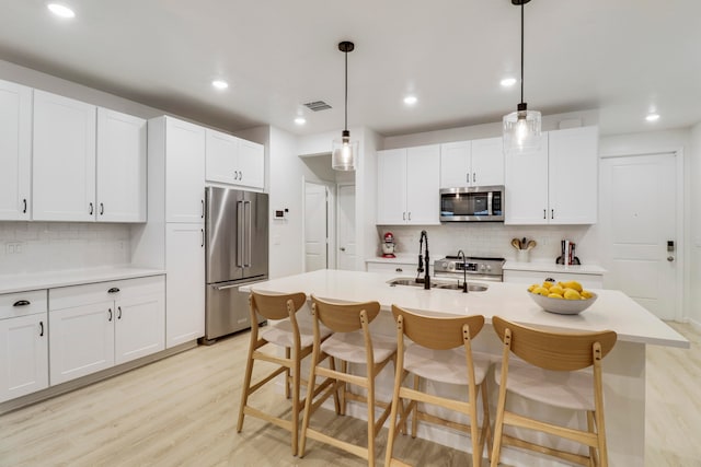 kitchen featuring a center island with sink, appliances with stainless steel finishes, light wood-type flooring, decorative light fixtures, and sink