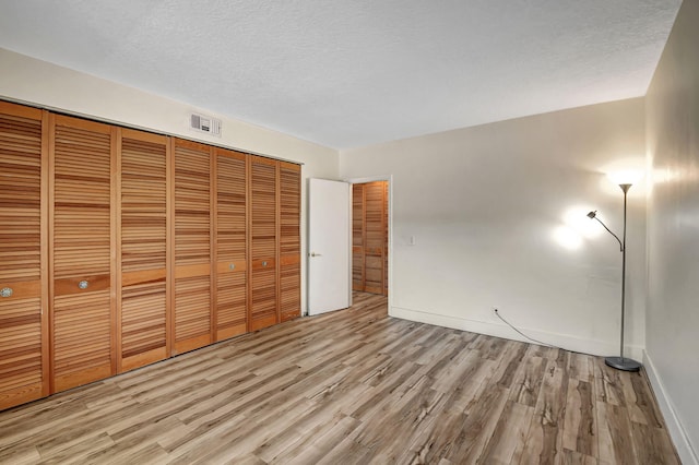 unfurnished bedroom featuring a textured ceiling, a closet, and light wood-type flooring