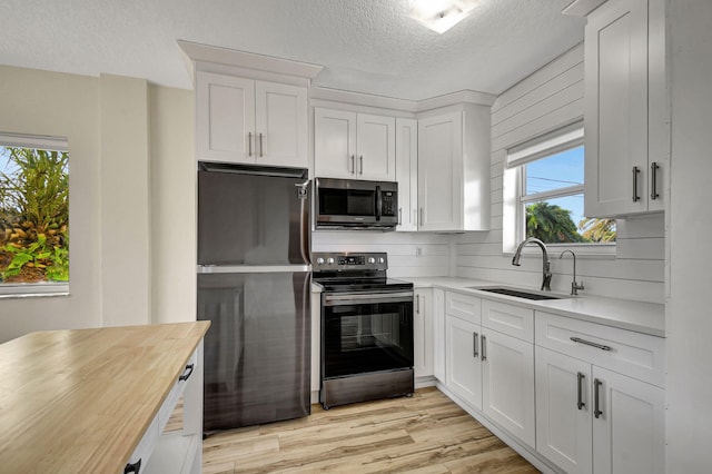 kitchen with light hardwood / wood-style floors, butcher block counters, stainless steel appliances, and white cabinets