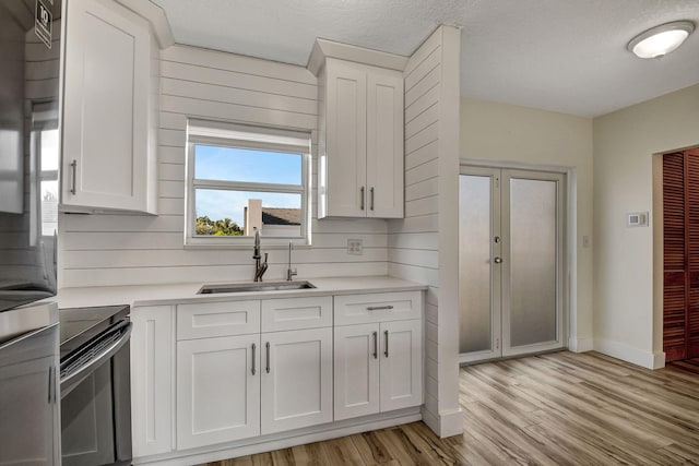 kitchen with sink, white cabinetry, wood walls, light hardwood / wood-style flooring, and black range oven