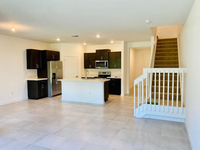 kitchen featuring appliances with stainless steel finishes, light tile patterned flooring, dark brown cabinetry, a center island with sink, and sink