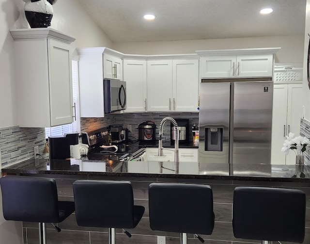 kitchen with stainless steel appliances, white cabinets, dark stone countertops, kitchen peninsula, and a breakfast bar area