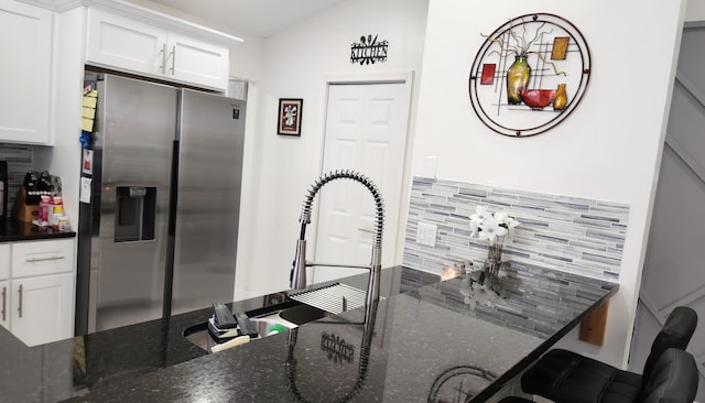 kitchen with lofted ceiling, decorative backsplash, stainless steel fridge, dark stone counters, and white cabinetry