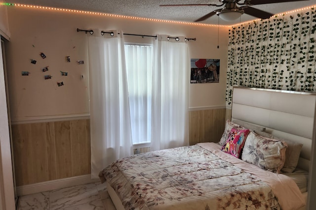 bedroom with ceiling fan, a textured ceiling, and wooden walls