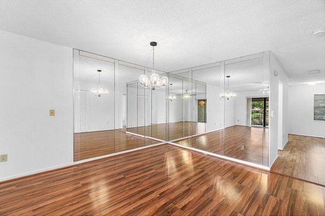 empty room with a textured ceiling, ceiling fan with notable chandelier, and hardwood / wood-style floors