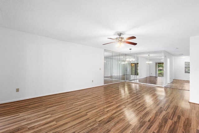 unfurnished living room featuring a textured ceiling, ceiling fan with notable chandelier, and dark hardwood / wood-style floors