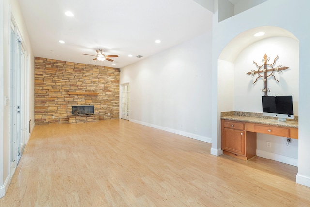 unfurnished living room featuring built in desk, a stone fireplace, ceiling fan, and light hardwood / wood-style flooring