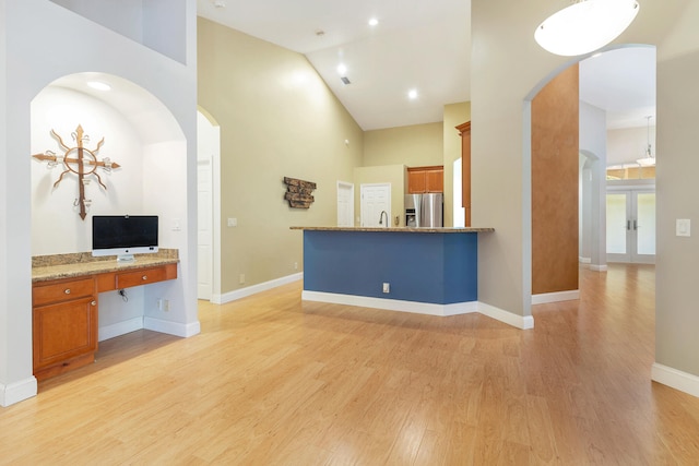 kitchen featuring stainless steel fridge, kitchen peninsula, built in desk, high vaulted ceiling, and light hardwood / wood-style floors