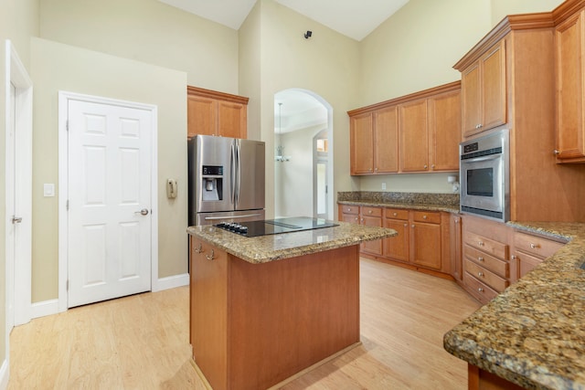 kitchen with light stone countertops, stainless steel appliances, a center island, and light hardwood / wood-style flooring