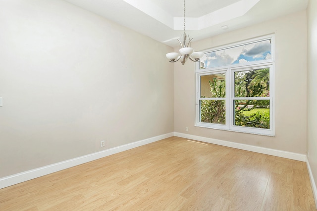 unfurnished room with a chandelier, light hardwood / wood-style floors, and a tray ceiling