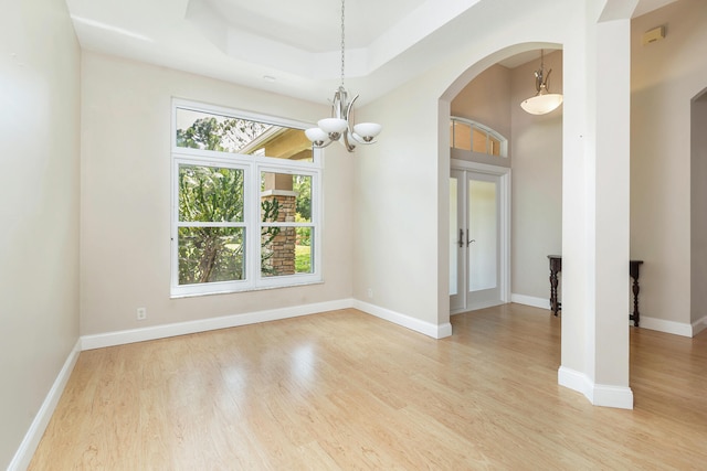 unfurnished room with an inviting chandelier, light hardwood / wood-style floors, and a raised ceiling