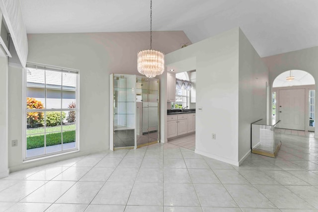 tiled empty room featuring vaulted ceiling, sink, a chandelier, and a wealth of natural light