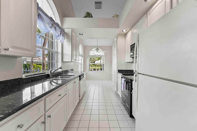 kitchen with dark stone countertops, white cabinetry, light tile patterned floors, black appliances, and sink