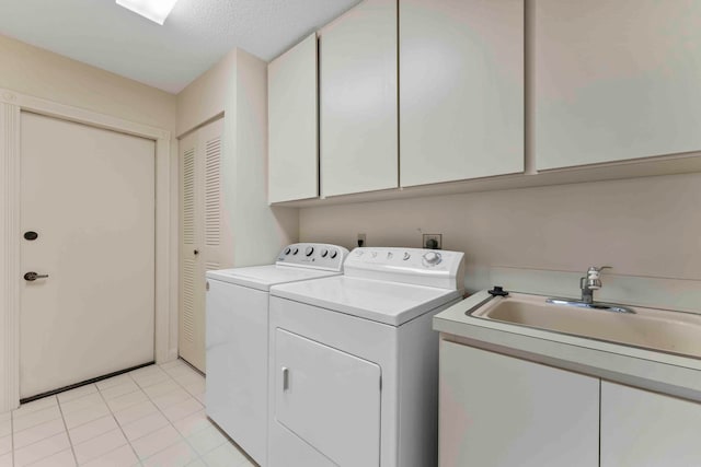 laundry area featuring light tile patterned flooring, a textured ceiling, cabinets, sink, and washer and dryer