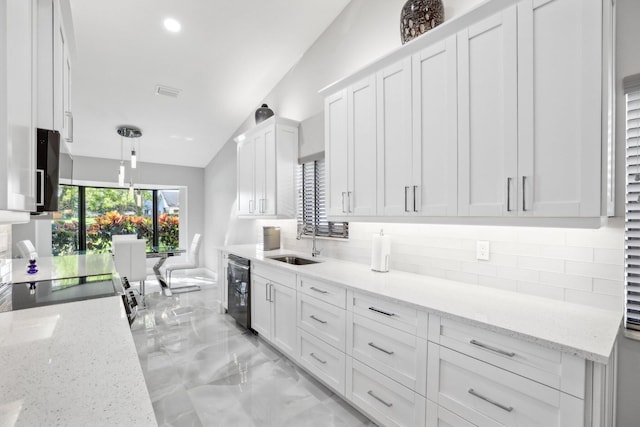 kitchen featuring pendant lighting, white cabinets, lofted ceiling, and light stone countertops