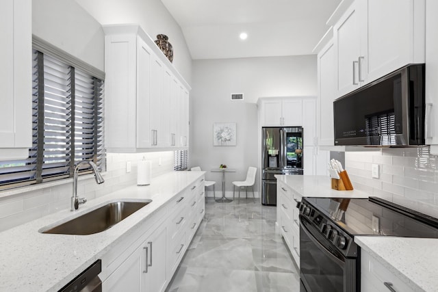 kitchen with sink, white cabinetry, black appliances, backsplash, and light stone countertops