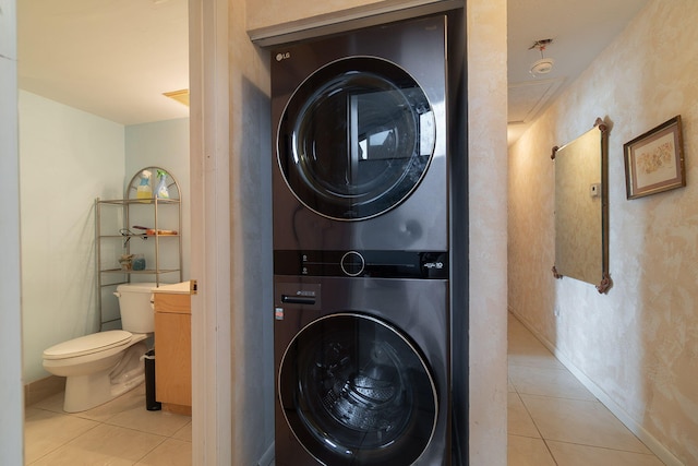 clothes washing area with stacked washer / drying machine and light tile patterned floors