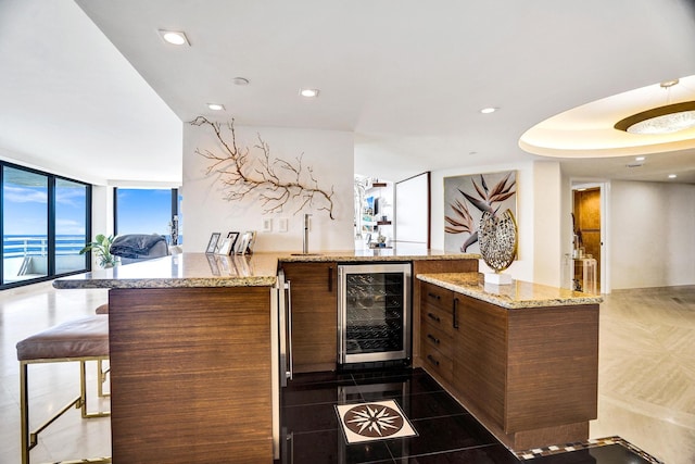 kitchen with dark tile patterned flooring, beverage cooler, light stone counters, and a wall of windows