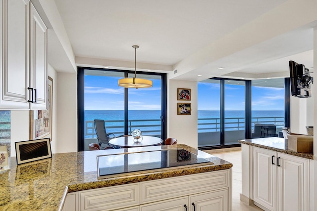 kitchen with black electric stovetop, white cabinets, hanging light fixtures, a water view, and dark stone countertops