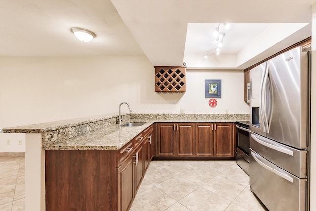 kitchen featuring kitchen peninsula, appliances with stainless steel finishes, rail lighting, light stone counters, and sink