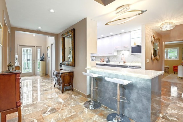 bar with backsplash, white cabinetry, sink, and a chandelier