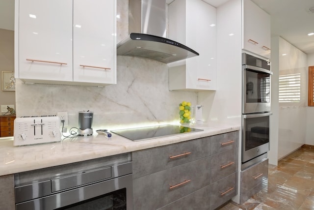 kitchen featuring white cabinets, black electric cooktop, double oven, and wall chimney exhaust hood