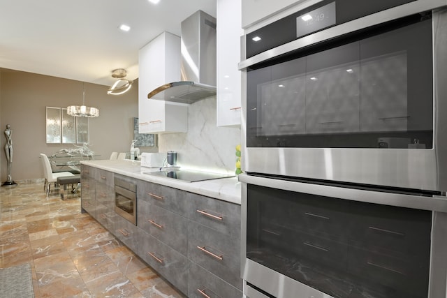 kitchen featuring hanging light fixtures, wall chimney exhaust hood, appliances with stainless steel finishes, tasteful backsplash, and light stone counters