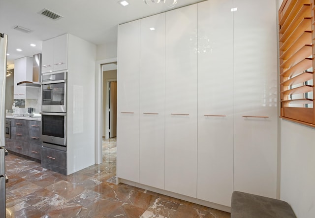 kitchen featuring double oven, wall chimney exhaust hood, and white cabinets