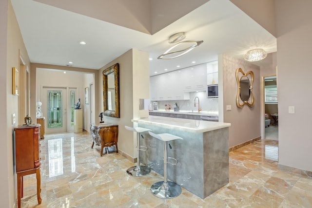 kitchen with kitchen peninsula, decorative backsplash, a breakfast bar, sink, and white cabinetry