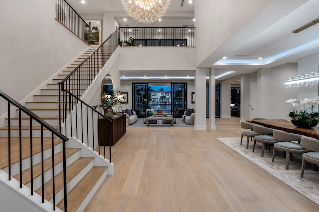 entryway featuring light hardwood / wood-style floors, a chandelier, a tray ceiling, and a towering ceiling