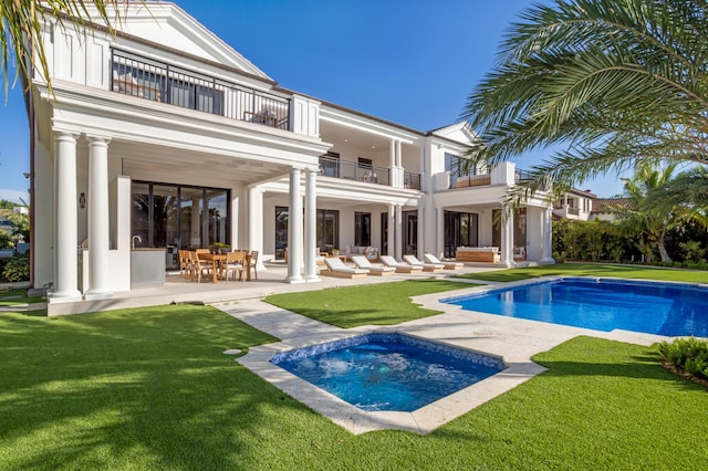 back of property with a patio, a pool with hot tub, a balcony, and a lawn