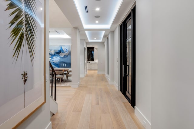 corridor with light hardwood / wood-style floors and a raised ceiling