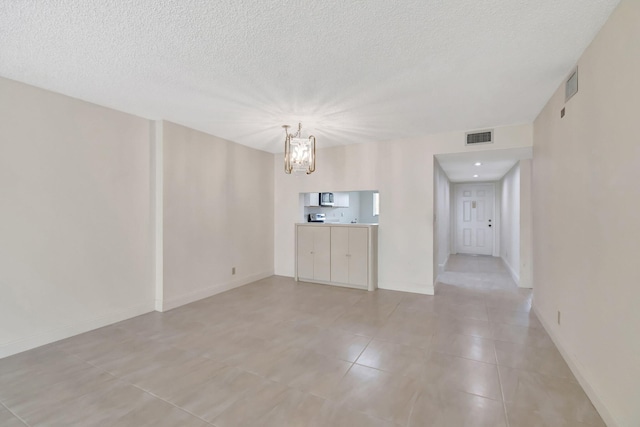 tiled empty room with a notable chandelier and a textured ceiling