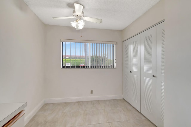 unfurnished bedroom with ceiling fan, light tile patterned flooring, a closet, and a textured ceiling