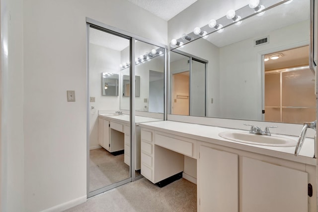 bathroom with a shower with shower door, vanity, and a textured ceiling