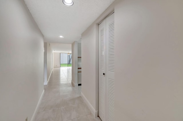 corridor with a textured ceiling and light tile patterned flooring