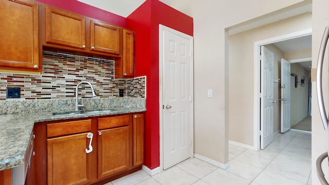 kitchen with sink, tasteful backsplash, light stone counters, stainless steel fridge, and light tile patterned floors